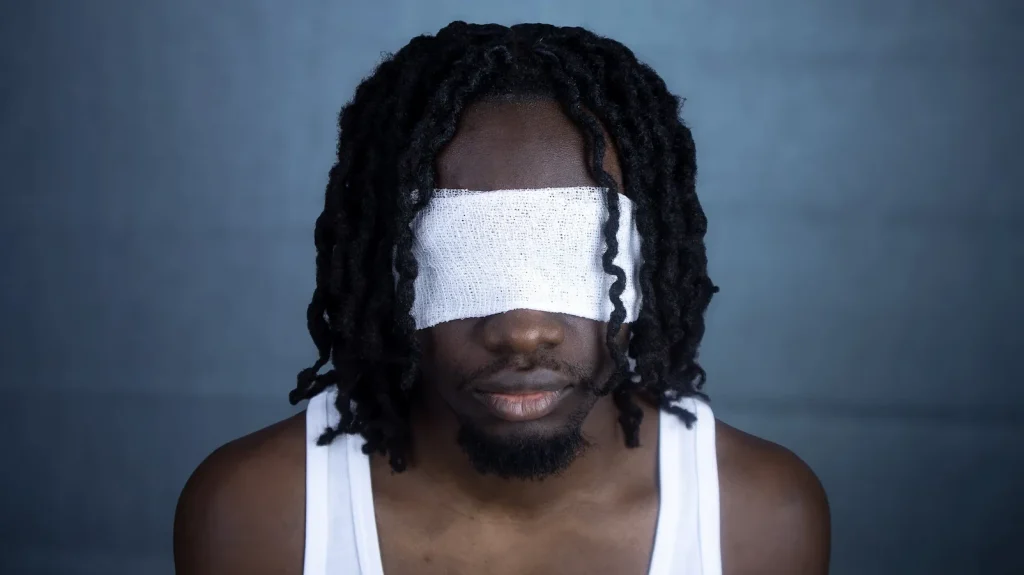Mann mit verbundenen Augen, Oberkörper sichtbar, vor blauem Hintergrund